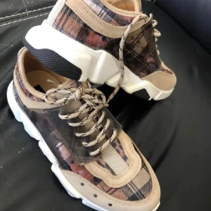 Rutig skinn sneakers från Blue on Blue 39 nya - Snygga skinn sneakers med ett unikt rutigt mönster i beige, svart och brunt. Skorna har snörning och en chunky vit sula som ger en modern look. Perfekta för dig som vill sticka ut med stil.