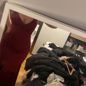 Röd  balklänning med öppen rygg och snörning - Säljer min balklänning köpt från NK. Klänningen har en  slits framtill och öppen rygg med  snörning. Orginalpris 3000kr