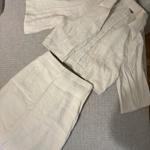 Beige linneset från Gina Tricot - Säljer en stilren beige set från Gina Tricot i linneblandning. Setet består av en kavaj med kortare passform och vida ärmar samt en matchande kjol med rak siluett. Perfekt för en fräsch och avslappnad look.