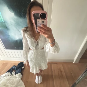 Vit spetsklänning med volang och v-ringning - Superfin vit klänning med spetsdetaljer, v-ringning och volang nertill. Klänningen har långärmade puffärmar, markerad midja med utskurna partier och broderade detaljer framtill. Perfekt för sommarens alla tillfällen. Helt ny köpt från raglady 