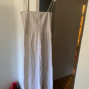 Vit långklänning från Boohoo - Säljer en vit långklänning från Boohoo med smala axelband och smockad överdel. Klänningen har en luftig och flowy passform, perfekt för varma dagar. Aldirg använd, enbart testad. 
