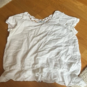 Vit blus med spetsdetaljer från Gina Tricot - Säljer en söt vit blus från Gina Tricot i storlek 36. Blusen har fina spetsdetaljer vid halsringningen och ryggen samt korta ärmar 
