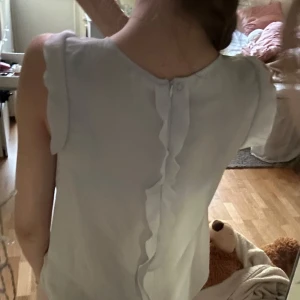Ljusblå blus med volangdetaljer - Säljer en söt ljusblå blus med volangdetaljer längs ärmhålen och ryggen.Pris går att diskutera!!!