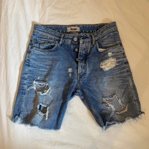 Blå slitna  jorts från Acne - Säljer ett par blå jeansshorts från Acne med råa kanter och flera slitningar framtill. I strl s 