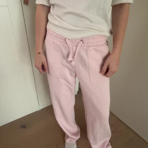 Ljusrosa mjukisbyxor med snörning - Säljer ett par ljusrosa mjukisbyxor med resår och snörning i midjan. Byxorna har raka ben och två fickor bak. Perfekta för en avslappnad stil.