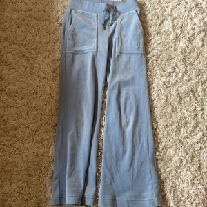 Ljusblå mjukisbyxor från Juicy Couture - Säljer ett par ljusblå mjukisbyxor från Juicy Couture med bred resår i midjan och dragsko. Byxorna har raka, vida ben, stora fickor fram och bak samt broderad logga på ena fickan. Perfekta för en avslappnad stil. Har sytts upp hos en skräddare, så dem är nu 85 cm långa. Orginalpris 1300kr. Pris kan diskuteras 💗