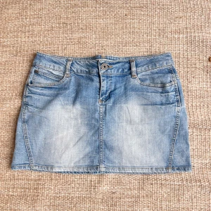 Ljusblå jeanskjol från ONLY - Säljer en klassisk ljusblå jeanskjol från ONLY med femficksmodell och knapp- samt dragkedjestängning framtill. Kjolen har bälteshällor och bakfickor med en liten röd detalj. Perfekt till sommargarderoben!