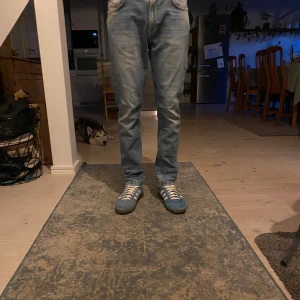 Ljusblå jeans från Nudie Jeans - Säljer ett par klassiska ljusblå jeans från Nudie Jeans med raka ben och snygga detaljer på bakfickorna. Jeansen har normal passform och är perfekta för en avslappnad stil. Midjan är midwaist och materialet är 100% denim. Det är en liten bit längst ner på båda jeansen som är på sydda men det syns knappt (kolla bilderna)