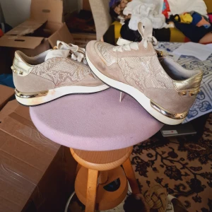 Beige sneakers med gulddetaljer från DLSport - Snygga beige sneakers från DLSport med glittriga partier och guldfärgade detaljer på häl och sula. Skorna har snörning, dragkedja på sidan och rund tå. Perfekta för dig som vill ha en sportig men trendig look.