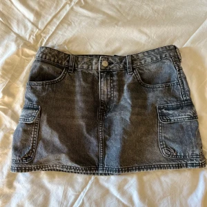 Svart jeanskjol med fickor - Säljer en svart jeanskjol i minilängd med cool fickdetalj på sidorna. Kjolen har bälteshällor och synliga sömmar för en snygg look. Perfekt att styla med sneakers eller boots. Oanvänd!🎀