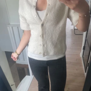 Vit stickad kofta från gina tricot - Säljer en söt vit stickad kofta från gina tricot med korta ärmar och knappar framtill. Koftan har en rak passform och ribbad struktur, perfekt att slänga över ett linne eller bara ha som t-shirt.