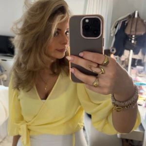 Gul omlottopp med knyt - Säljer en ljusgul omlottopp med knyt i sidan och v-ringad halsringning. Toppen har långa ärmar och är perfekt för dig som vill ha en fräsch och somrig look.
