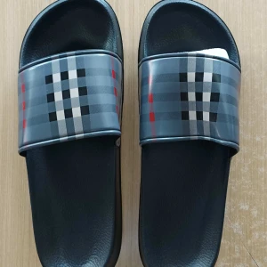 Svarta sandaler med rutigt mönster - Säljer ett par svarta burberry sandaler med bred rem i klassiskt rutigt mönster i grått, vitt, svart och röda detaljer. Perfekta för sommaren och enkla att glida i. Snygg och stilren design som passar till många outfits.