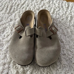  Birkenstock Boston taupe 42 - Säljer ett par klassiska Birkenstock Boston storlek 42 i beige (taupe) mocka med justerbart spänne i metall. Endast använda ett par gånger inomhus.
