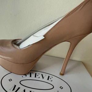 Beiga pumps med platå från Steve Madden - Säljer ett par snygga beiga pumps från Steve Madden i modellen Allyy. Skorna har hög klack och platåsula, rund tå och är tillverkade i syntetmaterial. Perfekta för dig som vill ha ett par eleganta och trendiga klackar.