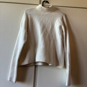 Vit stickad polotröja - Säljer en vit stickad polotröja med hög krage och långa ärmar. Tröjan har bred ribbstickning vid krage, ärmslut och nederkant. Perfekt för kyliga dagar och enkel att matcha med olika outfits.