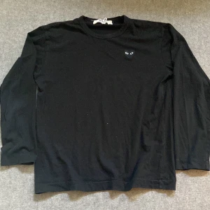 Svart långärmad tröja från Comme des Garçons Play - Säljer en svart långärmad tröja från Comme des Garçons Play med det ikoniska hjärta med ögon broderat på bröstet. Tröjan har en klassisk passform och är gjord i mjuk bomull. Perfekt för en stilren och enkel look. Storlek L men passar mer M