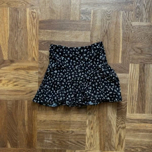 Svart blommig byxkjol  - Supersöt svart byxkjol från Zara med vitt blommönster. Kjolen har en lätt utsvängd form och är kort i modellen. Perfekt att styla med en enkel topp eller stickad tröja. Materialet känns mjukt och flowy. Väldigt bra skick. 
