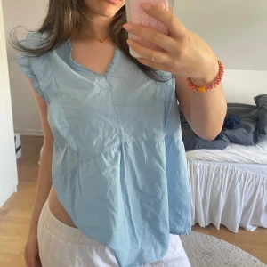 Ljusblå blus med volangärmar - NYTT SKICK (aldrig använd) Säljer en ljusblå blus med volangdetaljer vid ärmarna och v-ringad hals. Blusen är tillverkad i ett tunt, lätt material och har en avslappnad passform. Perfekt för varma dagar! Strl s/m 