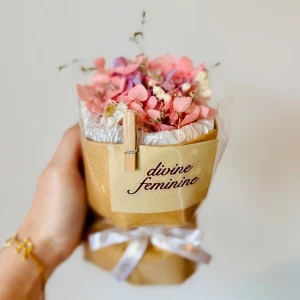 torkade blommor -  en bukett med torkade blommor i rosa och lila toner, inslagna i brunt papper och dekorerad med en vit rosett. På pappret sitter en etikett med texten 'divine feminine'.