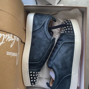 Mörkblåa sneakers med nitar från Christian Louboutin - Säljer ett par äkta Christian Louboutin sneakers i mycket fint skick.Mockan är i nyskick och välbevarad. Sulorna är använda men går enkelt att rengöra. På insidan av skorna har en liten del av märkets namn börjat försvinna, men detta påverkar inte skornas utseende eller komfort. Du får även med alla tillbehör som var med paketet.Pris kan diskuteras och autenticitet finns på sista bilden, kvitto får du via min plick.                               Ny pris:10000kr.