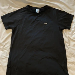 Svart träningst-shirt från ICANIWILL - Säljer en svart kortärmad t-shirt från ICANIWILL. Perfekt för träning med lätt och ventilerande syntetmaterial. Diskret logga på bröstet och klassisk passform. Finns ett litet synligt skada vid bröstet. Annars bara använt ett fåtal gånger. Säljer då passformen inte passade mig.