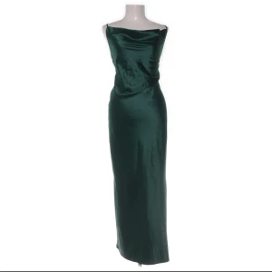 Grön långklänning med smala axelband - Elegant långklänning i djupgrön färg med smala korsade axelband och draperad halsringning. Klänningen har en slät, glansig yta och är figurnära med en lätt slits. Perfekt för speciella tillfällen. Okänt märke, aldrig använd av mig, då den inte passade 💗 hör av er vid frågor 💗priset är diskuterbart vid snabb affär 