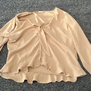 Beige blus från Vila i storlek 42 - Jag säljer en volangig beige blus från Vila i storlek 42. Man kan knyta den där fram och har även några knappar som man knäpper på framsidan. Perfekt för dig som gillar att styla en tröja med fina smycken och ett par jeans