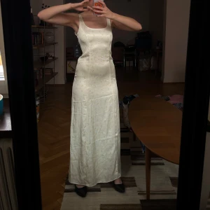 Ljusgul långklänning med blommigt mönster - Ny med prislappar kvar, slutsåld på na-kd! Ljusgul långklänning med blommigt mönster och fin snörning i ryggen. Klänningen är i satinliknande material. Perfekt för student och bal!