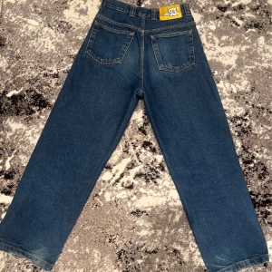 Blå wide jeans från 99DENIM - Säljer ett par blå jeans från 93 DENIM med raka, vida ben och klassisk femficksdesign. Jeansen har en broderad detalj vid fickan och patch bak i midjan. Perfekta för dig som gillar en avslappnad och trendig stil.