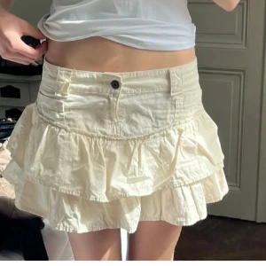 Mini kjol - Säljer en söt vit kjol från Bershka med två volanglager och knapp framtill. Kjolen har fickor och är i en kort modell som passar perfekt till sommaren. Enkel att matcha med olika toppar för en fräsch look. Storlek 38😊