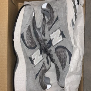 Grå New Balance 2002R sneakers - Säljer ett par grå New Balance 2002R sneakers med meshpaneler och mockadetaljer. Skorna har en vit och svart sula, klassisk N-logga på sidan och snörning framtill. Perfekta för dig som gillar stilrena och bekväma sneakers.