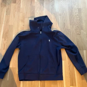 Mörkblå Ralph Lauren zip hoodie - Säljer en mörkblå hoodie från Polo Ralph Lauren i storlek M.  Tröjan är i bra skick och inte använt många gången alls , mitt priss 400 men kan diskuteras vid bara snabb affär !