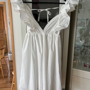 Somrig vit klänning - En söt kort vit klänning i poplin perfekt till studenten! Helt i nyskick med tagg från Club L London. Jag är 161 lång och den går till knäna. Kortärmad med knytdetalj i ryggen. Storlek EUR 40 (UK 12)