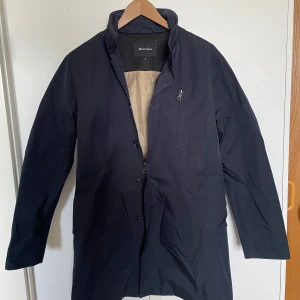 Svart rock från Martinique - Stilren svart rock från Matinique med knappar och dragkedja framtill. Lätt fodrad insida i beige och hög krage. Perfekt för dig som vill ha en klassisk och enkel look.