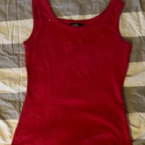 Röd linnetopp med paljetter från Isolde - Säljer en röd topp från Isolde med glittriga paljettdetaljer framtill. Perfekt för dig som vill ha något färgstarkt och lite extra till din outfit. Linnet har en klassisk rund halsringning och är ärmlöst. Den är i storlek M men är insydd, skulle därför säga st S istället🥰🥰🥰