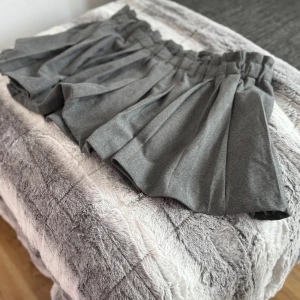 Grå plisserad kortkjol med resårmidja - Säljer en grå kortkjol med bred resår i midjan och plisserade veck. Kjolen har en klassisk och stilren look, perfekt för att matcha med olika toppar. Materialet känns mjukt och följsamt.