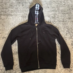 Burberry hoodie - Svart hoodie med mönster på insidan. Tröjan har dragkedja och snöre i luvan. Etikett och lappar sitter kvar. Perfekt till en mer avslappnad stil! Använd 2-3 gånger, passar som både M och L