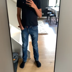 Mörkblått flätat bälte med bruna skinn-detaljer - Säljer ett mörkblått flätat bälte med snygga bruna skinn-detaljer vid spännet. Bältet har en flexibel och stilren design som passar till jeans eller chinos. Perfekt accessoar för att lyfta din outfit.