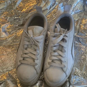 Vita sneakers från Puma - Säljer ett par klassiska vita sneakers från Puma med tjock sula och snörning. Skorna har rund tå och är tillverkade i syntetmaterial. Perfekta för dig som gillar en sportig och stilren look.