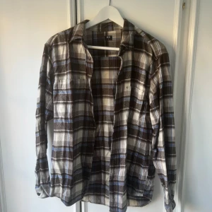 Rutig skjorta från Uniqlo - Säljer en rutig skjorta från Uniqlo i brunt, blått, vitt och grått. Skjortan har långa ärmar och knäppning framtill. Perfekt för dig som gillar en avslappnad stil.
