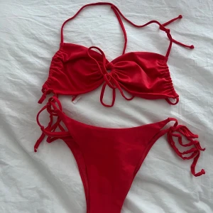 Röd bikini med knyt -  röd bikini med knyt både på överdel och underdel. Överdelen har smala axelband och rynkade detaljer framtill. Underdelen har högt skurna ben och knyt i sidorna för justerbar passform. Perfekt för stranden eller poolen. Inte använd