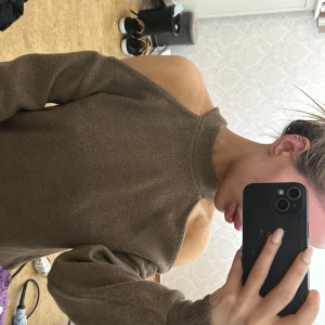 Brun offshoulder stickad tröja - Säljer en brun stickad tröja med offshoulder-design och hög hals. Tröjan har långa ärmar och en lös passform.