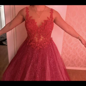 Rosa glittrig balklänning med spetsdetaljer - Säljer en rosa långklänning med glittrigt tyg och vackra spetsdetaljer upptill. Klänningen har öppen rygg, djup v-ringning och är ärmlös. Kjolen är voluminös och skimrar snyggt i ljuset – perfekt för bal eller fest.