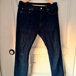 Mörkblå Levis jeans 501 - Snygga mörkblå jeans från Levis med klassisk femficksdesign och raka ben. Byxorna har kontrastsömmar och Levis ikoniska läderpatch bak i midjan. Passar perfekt till vardags och har en tidlös look.