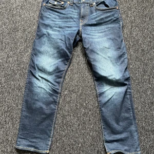 True religion brallor - Säljer ett par klassiska blå jeansbyxor från true religion i modellen Relaxed Straight. Jeansen har raka ben,  och snygga kontrastsömmar. Bakfickorna har dekorativa sömmar