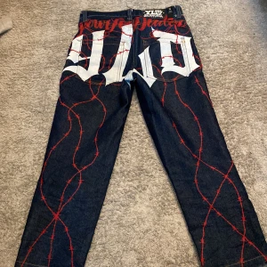 Mörkblå jeans med tryck från Your Local Dealer - Unika mörkblå jeans från Your Local Dealer med stora vita tryck och röda taggtrådsdetaljer på baksidan. Klassisk femficksmodell med knapp och dragkedja. Snygg broderad detalj vid fickan framtill. 