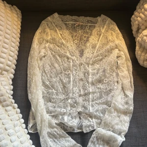 Vit spetsblus med v-ringning - Säljer en superfin vit spetsblus med v-ringning och långa ärmar. Blusen har ett vackert blommigt spetsmönster och är genomskinlig, perfekt att styla över ett linne eller bh. Passar dig som gillar romantisk och feminin stil. Stolek M