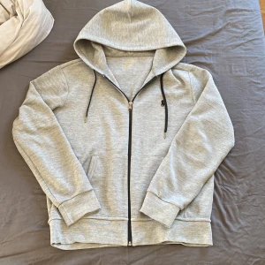 Grå hoodie med dragkedja från Polo Ralph Lauren - Säljer en klassisk grå hoodie från Polo Ralph Lauren med dragkedja och svart broderad logga på bröstet. Tröjan har huva med snörning och två fickor framtill. Perfekt för en avslappnad stil. Vid ytligare frågor är de bara att höra av sig, priset är inte hugget i sten. 