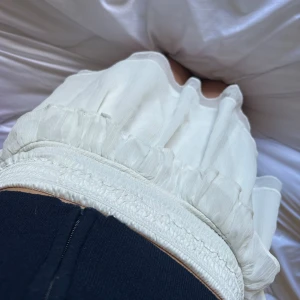 Vit volangkjol med smock i midjan - Supersöt vit kjol med volangdetaljer och bred smock i midjan. Kjolen är kort och har en luftig känsla, perfekt för varmare dagar. BRA FÖR DEN PASSAR ALLA KROPSFORMSR DÅ DEN är stretch💕